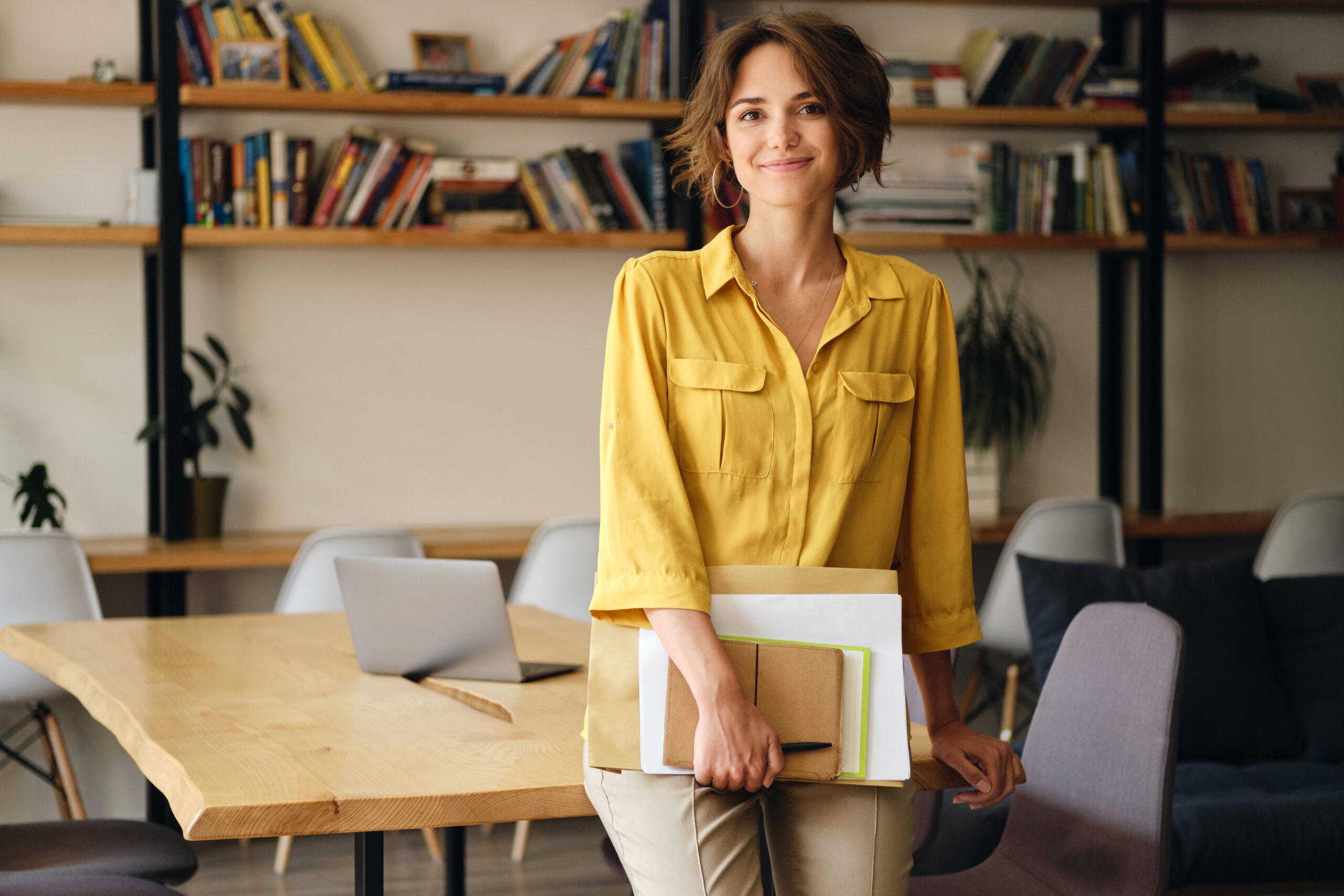 Young beautiful woman in yellow shirt leaning on desk with notep